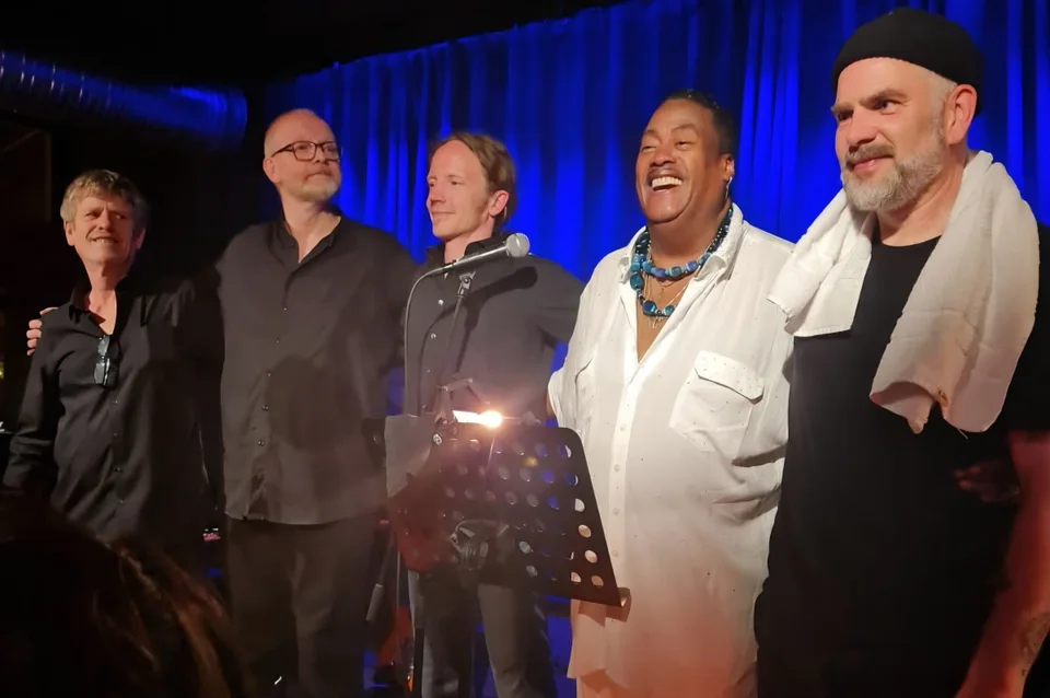 Keith with four musicians in front of a blue stage curtain